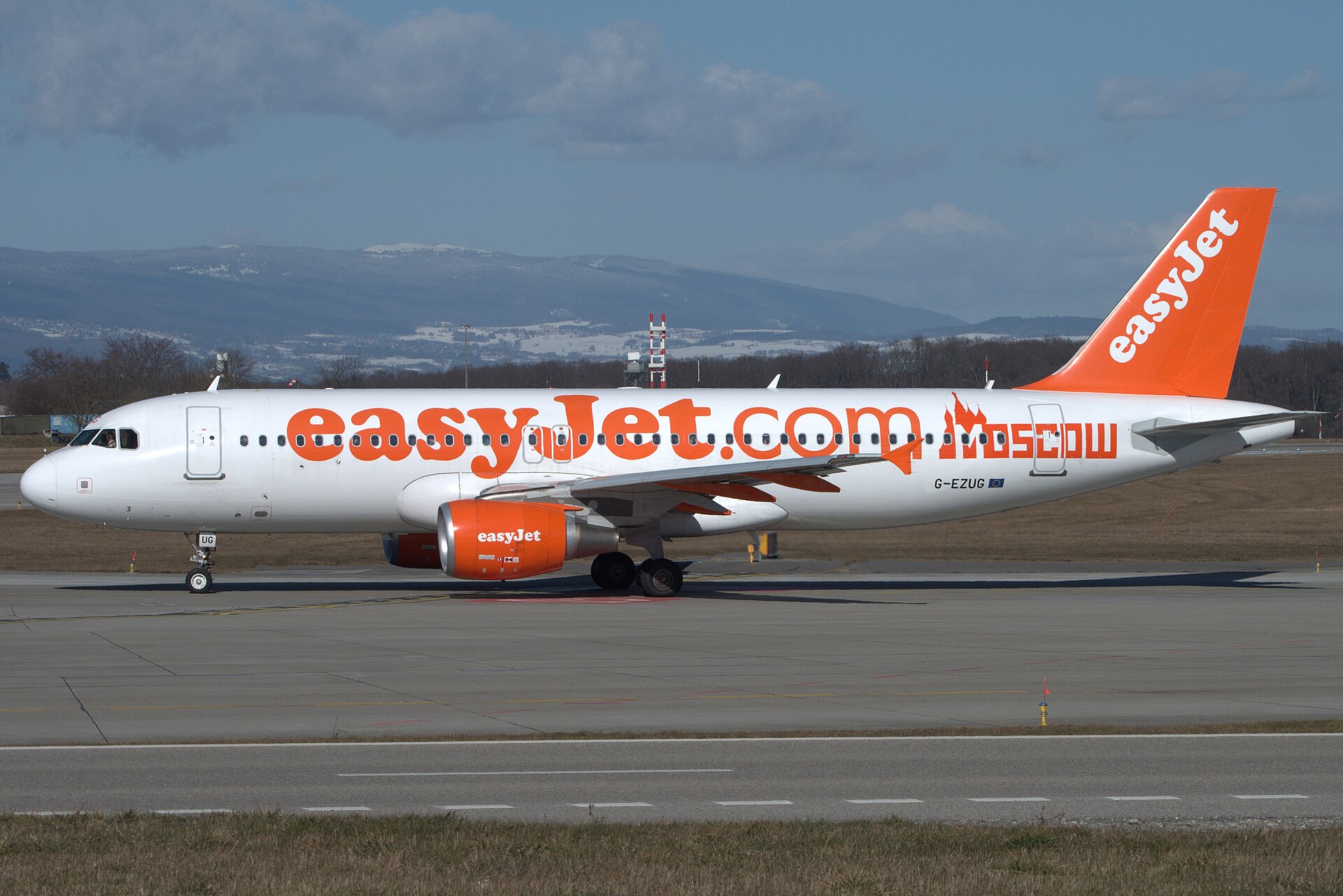 An easyJet Airbus A320 taxiing at Geneva Airport in winter with the snow-dusted Jura behind