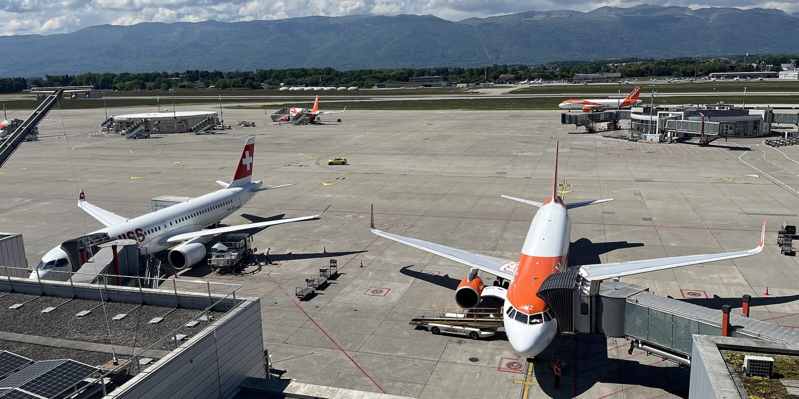 SWISS and easyJet aircraft at their gates at Geneva Airport, seen from the panorama terrace with the Jura mountains behind
