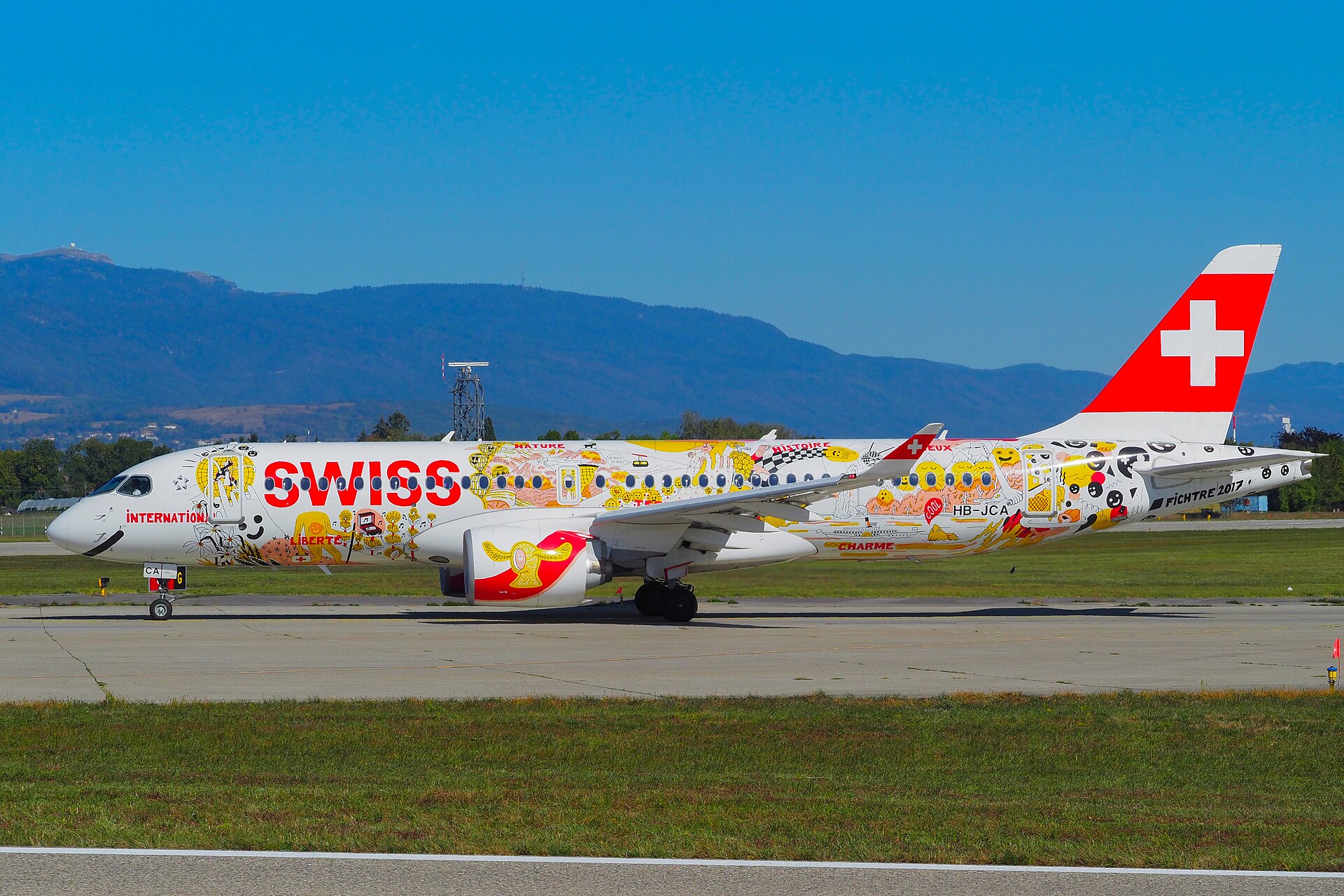 A SWISS Airbus A220 in a colourful special livery taxiing at Geneva Airport, with the Jura behind