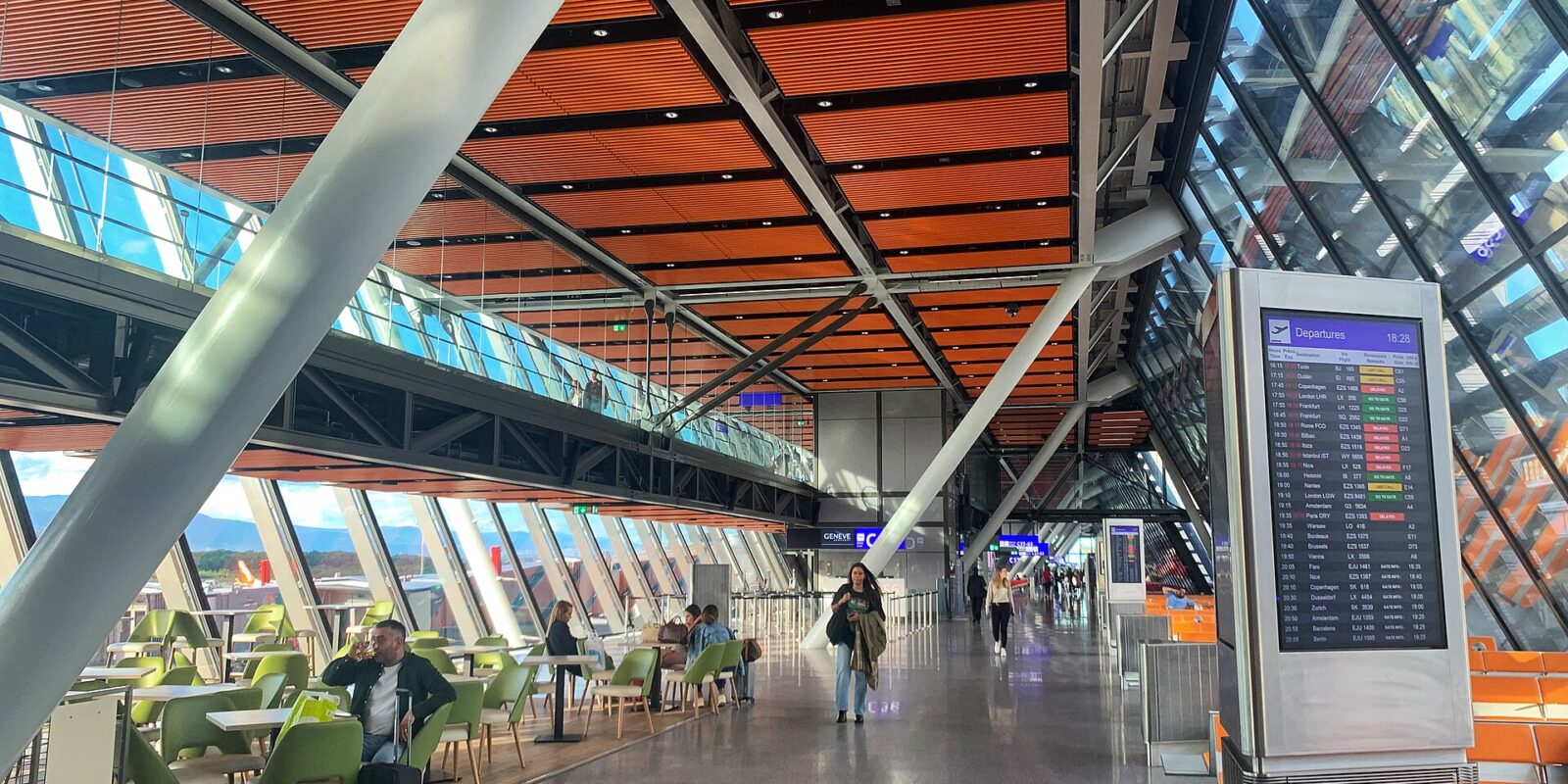 The glass and timber East Wing departures hall at Geneva Airport with a flight information board
