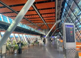 The glass and timber East Wing departures hall at Geneva Airport with a flight information board