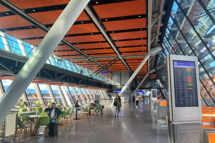The glass and timber East Wing departures hall at Geneva Airport with a flight information board