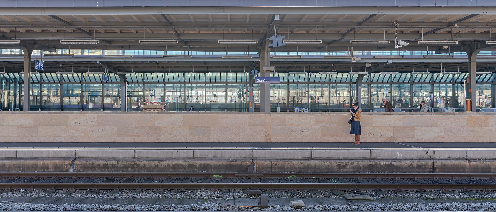 A platform at Genève-Cornavin station with the Genève sign and a passenger waiting