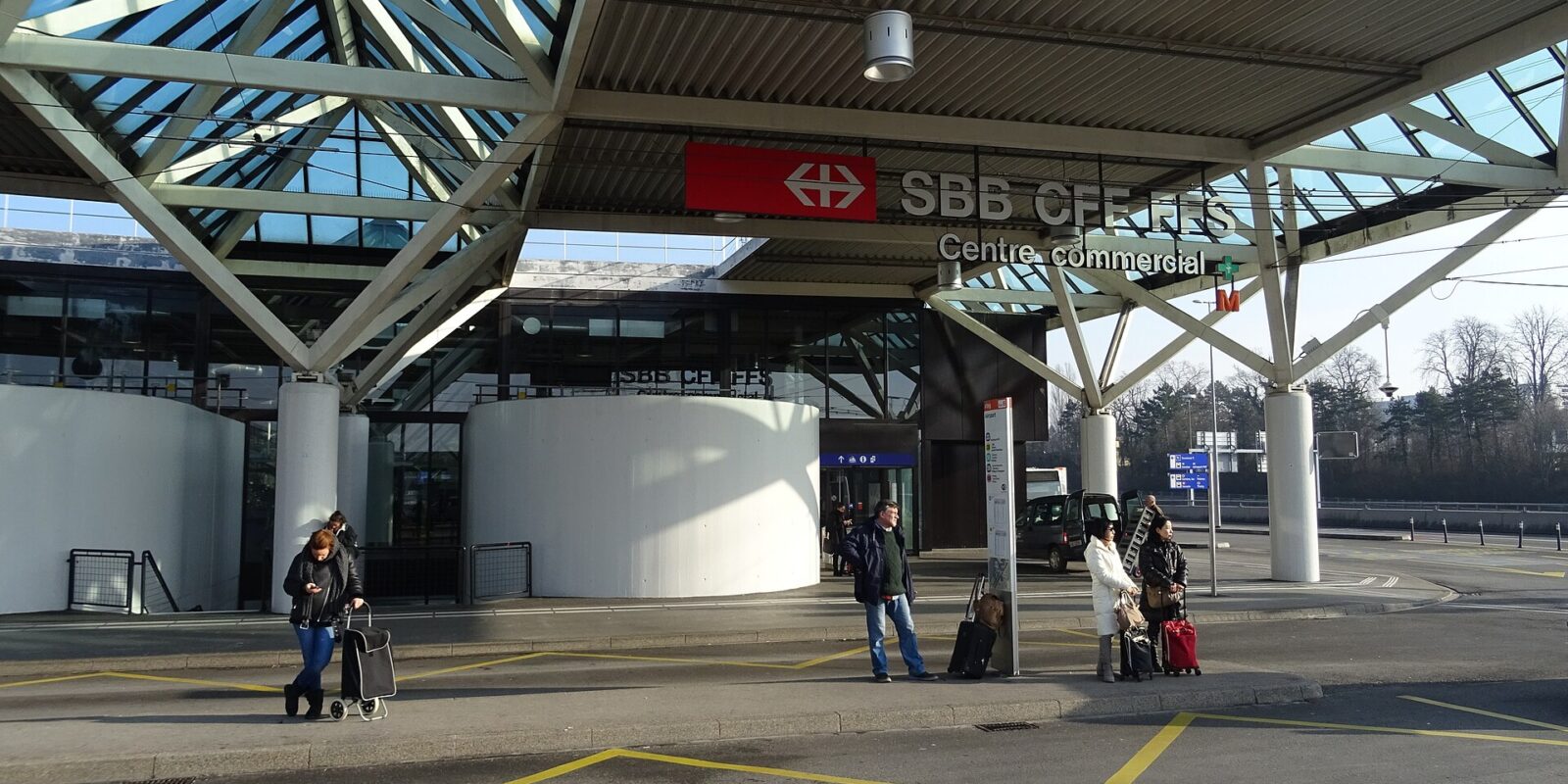 Travellers with suitcases waiting at the tpg bus stop outside the SBB railway station at Geneva Airport