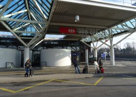Travellers with suitcases waiting at the tpg bus stop outside the SBB railway station at Geneva Airport