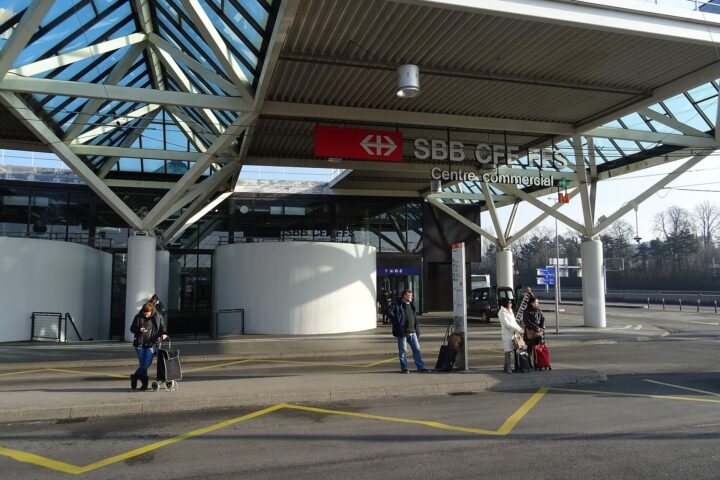 Travellers with suitcases waiting at the tpg bus stop outside the SBB railway station at Geneva Airport