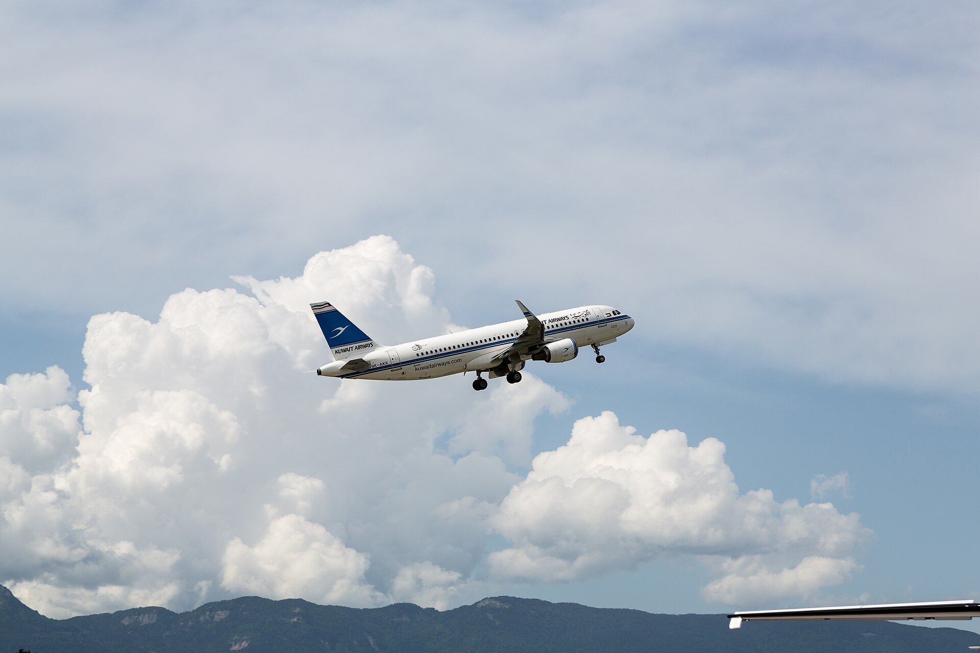 An Airbus A320 climbing away from Geneva Airport with cumulus cloud and hills behind