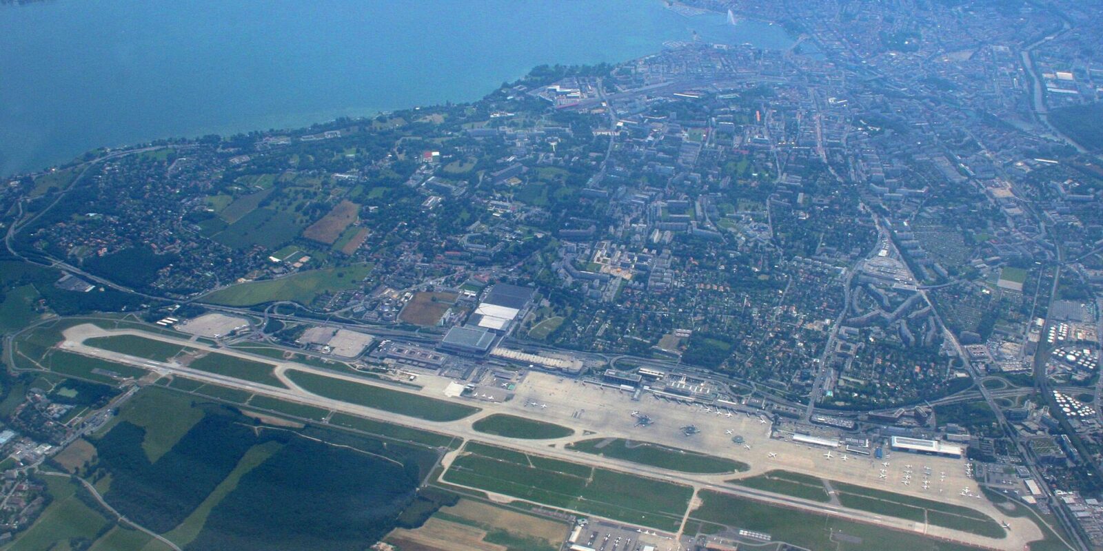 Aerial view of Geneva Airport's single runway with the city and Lake Geneva beyond