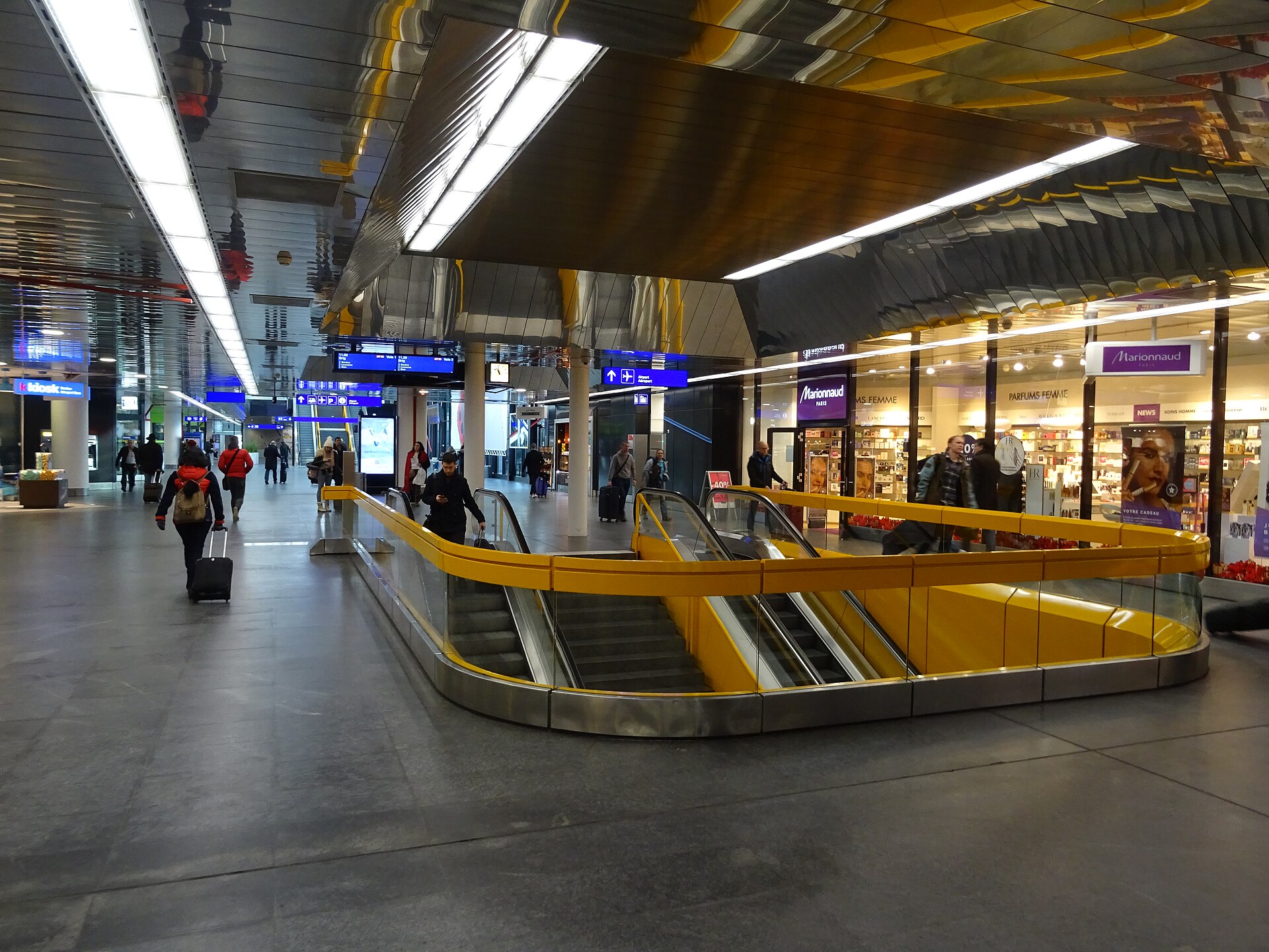The concourse of the Genève-Aéroport railway station with yellow-railed escalators leading down to the platforms