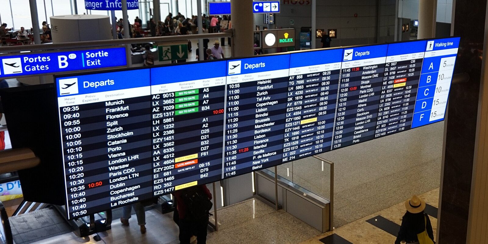 Geneva Airport departure boards showing flights and a walking-time panel for gates A, B, C, D and F