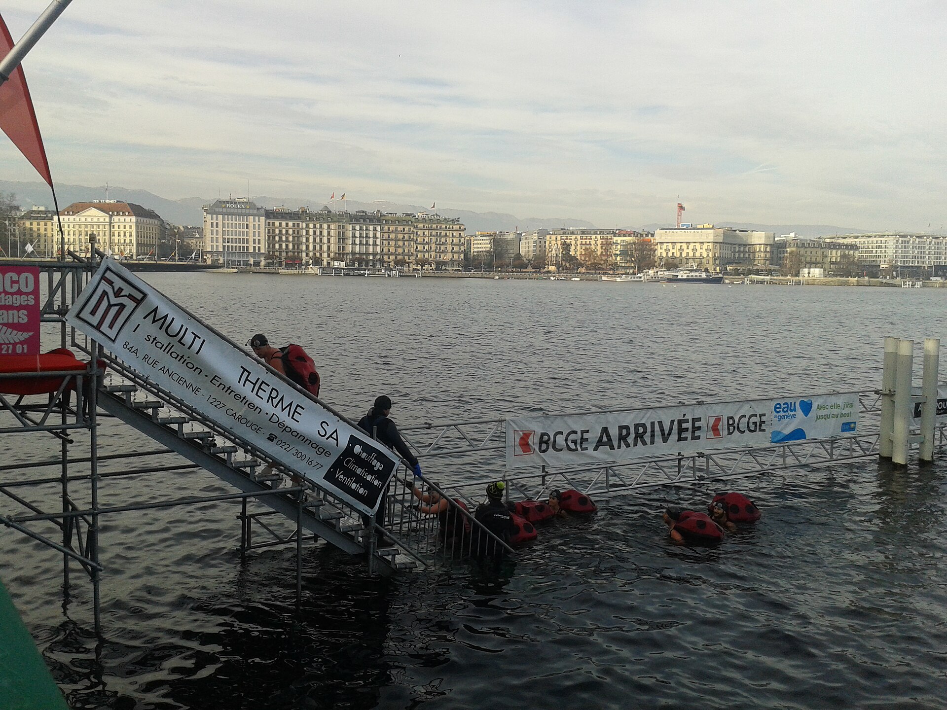 Swimmers in ladybird costumes at the finish of the Coupe de Noël in Lake Geneva, with the Quai du Mont-Blanc hotels behind