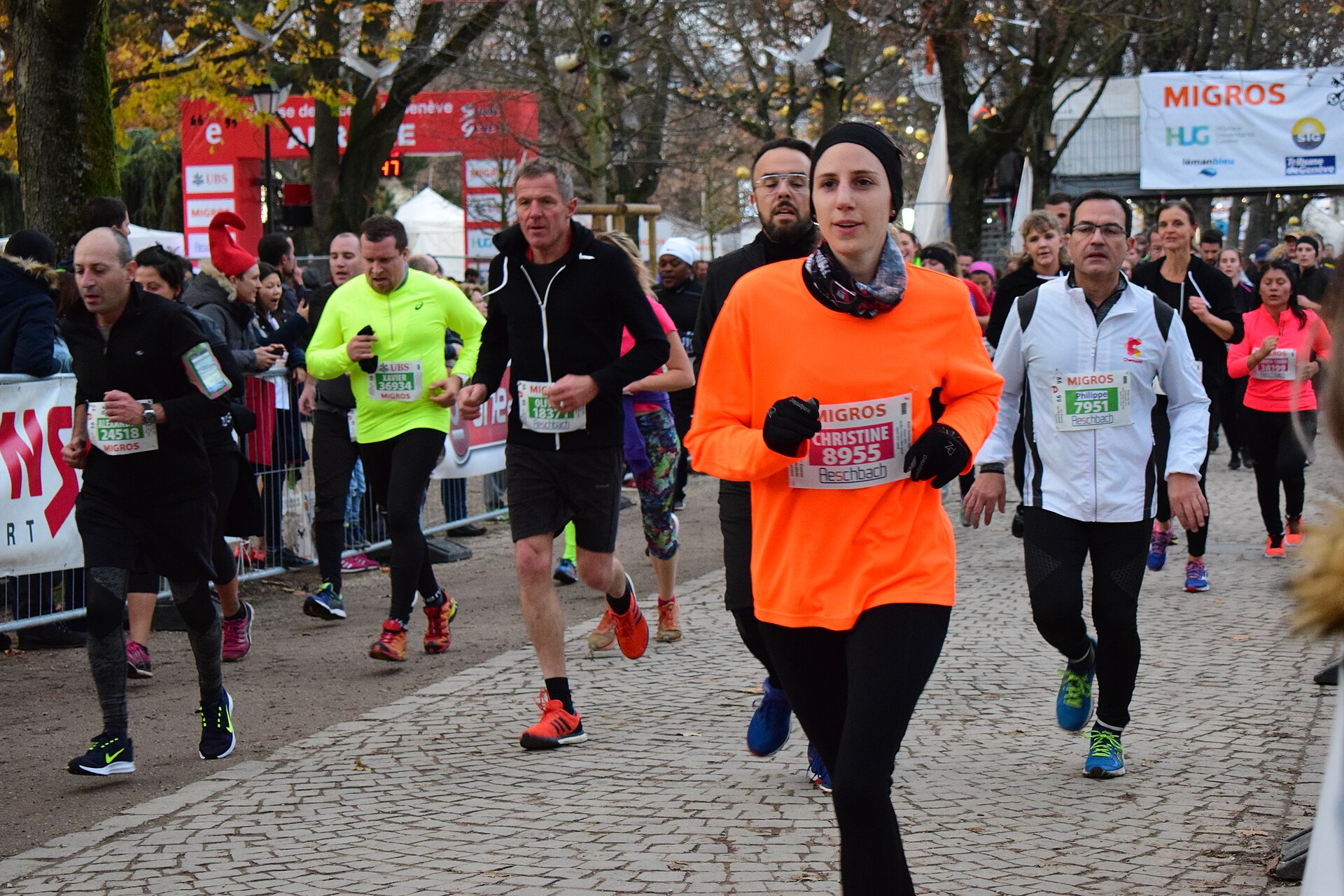 Runners with race numbers at the Course de l'Escalade on a cobbled path in the Parc des Bastions