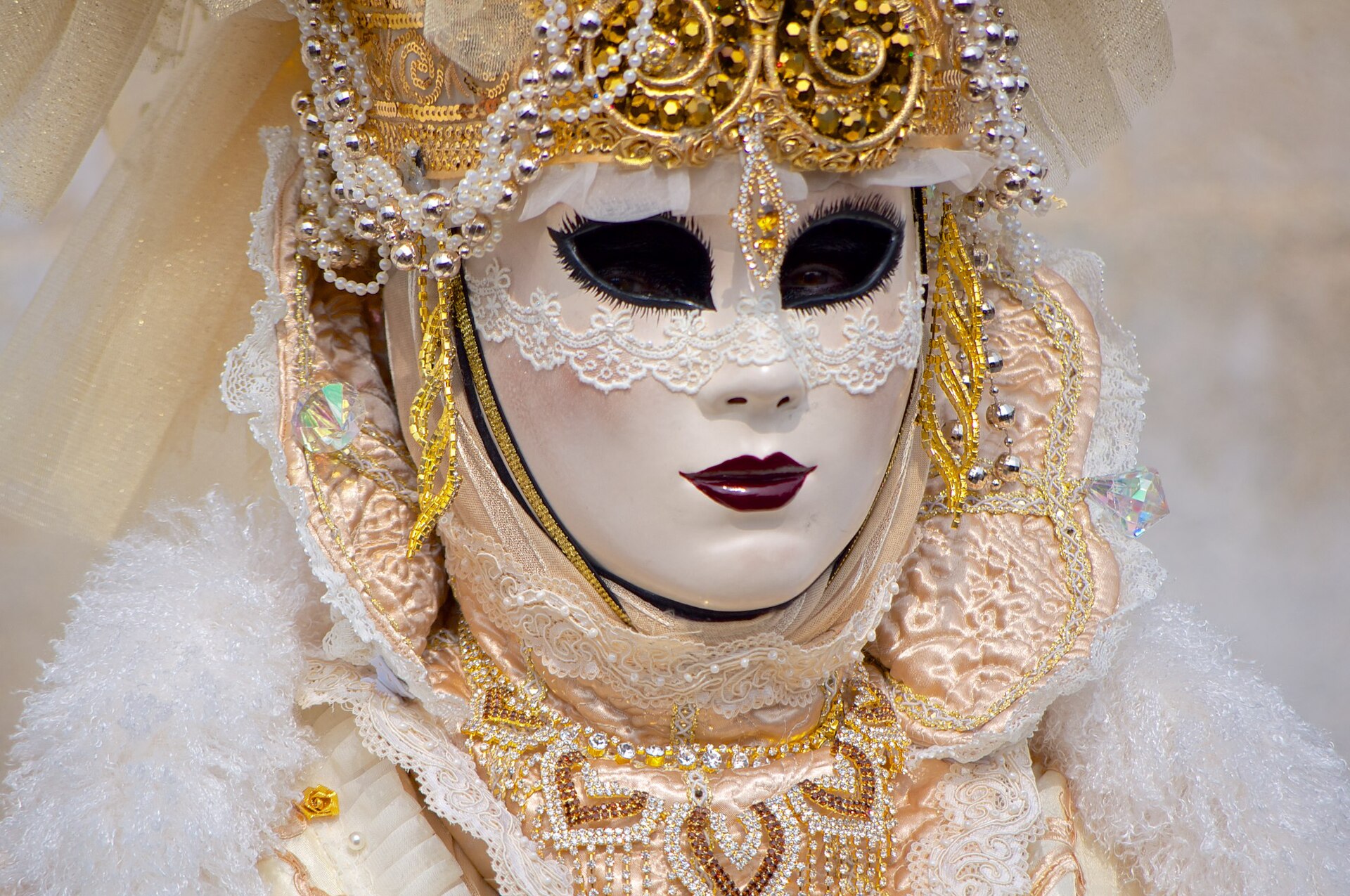 A figure in a white Venetian mask with a gold and pearl headdress at the Annecy Venetian Carnival