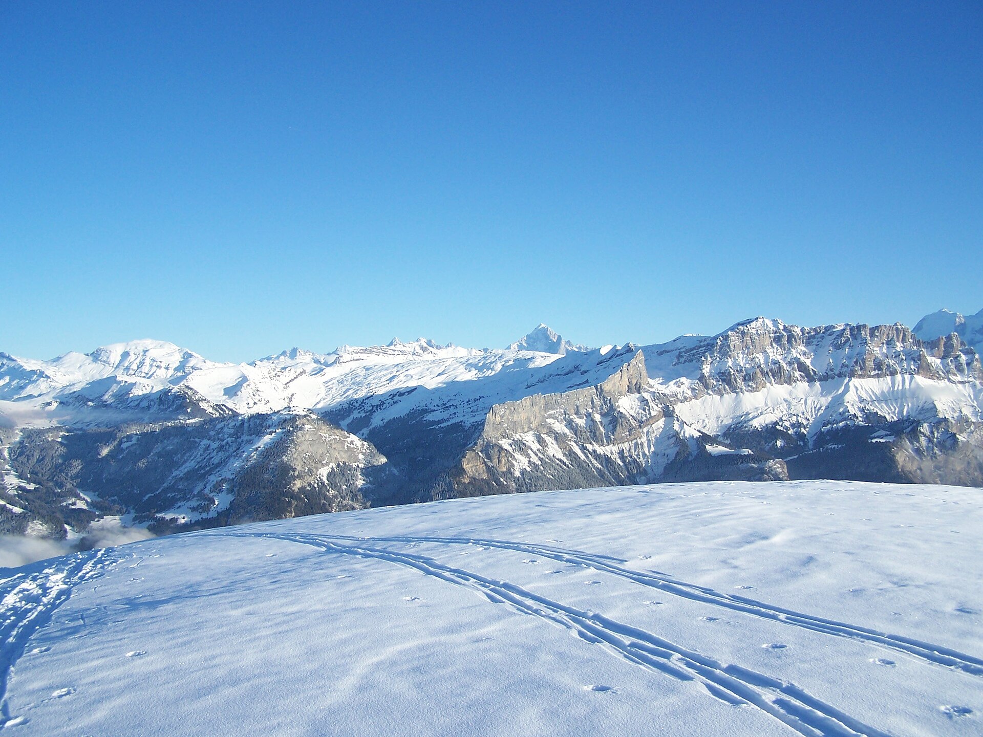 Ski tracks in fresh snow on the Grand Massif near Flaine, with the snow-covered Platières cliffs and the Buet under a clear blue sky