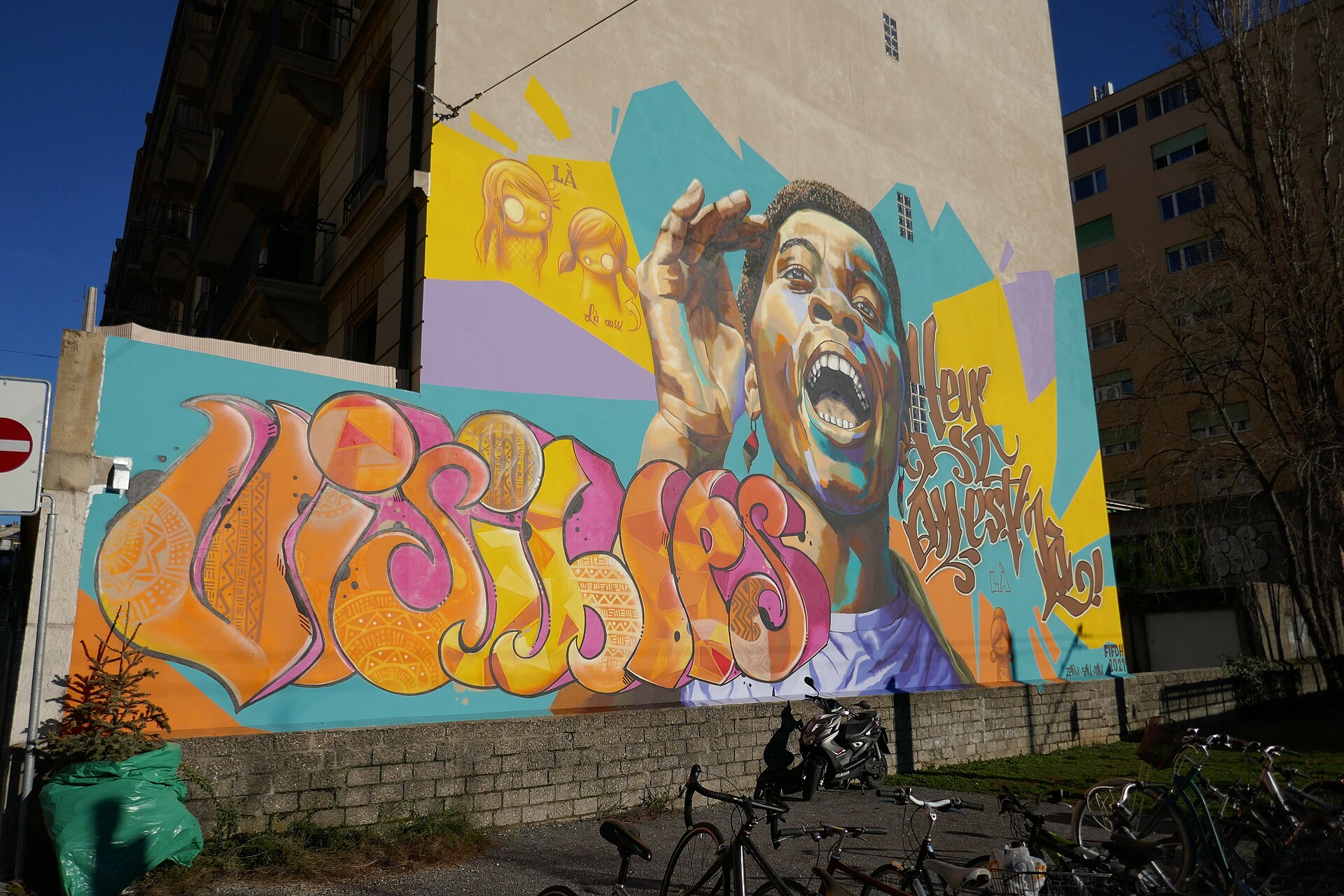 A large colourful street mural of a laughing young person on a Geneva building, signed FIFDH 2021
