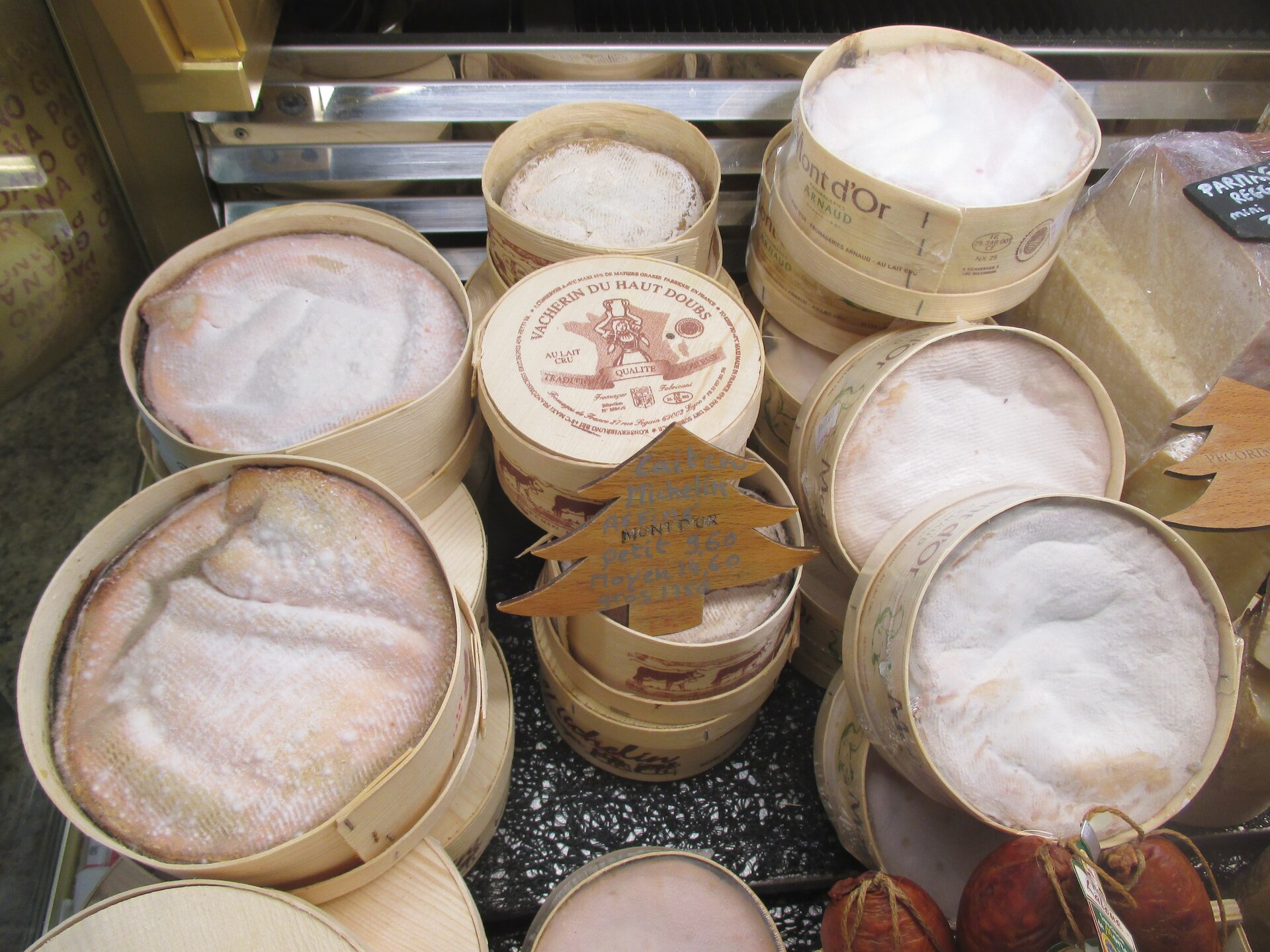 Round spruce boxes of Mont d'Or and Vacherin du Haut-Doubs cheese stacked on a cheese counter