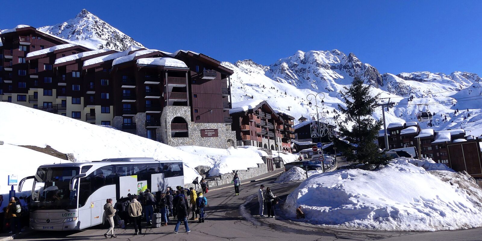 A transfer coach unloading passengers and luggage at a snow-covered French ski resort