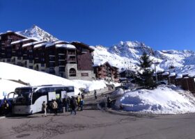 A transfer coach unloading passengers and luggage at a snow-covered French ski resort