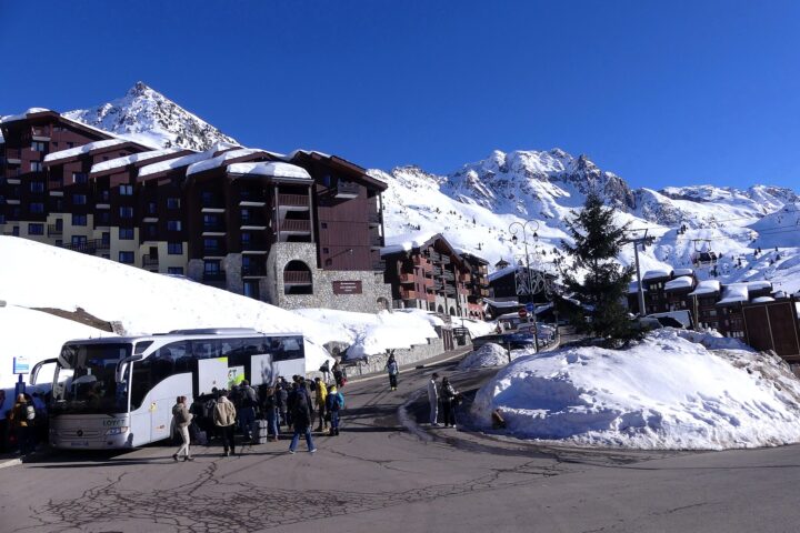 A transfer coach unloading passengers and luggage at a snow-covered French ski resort
