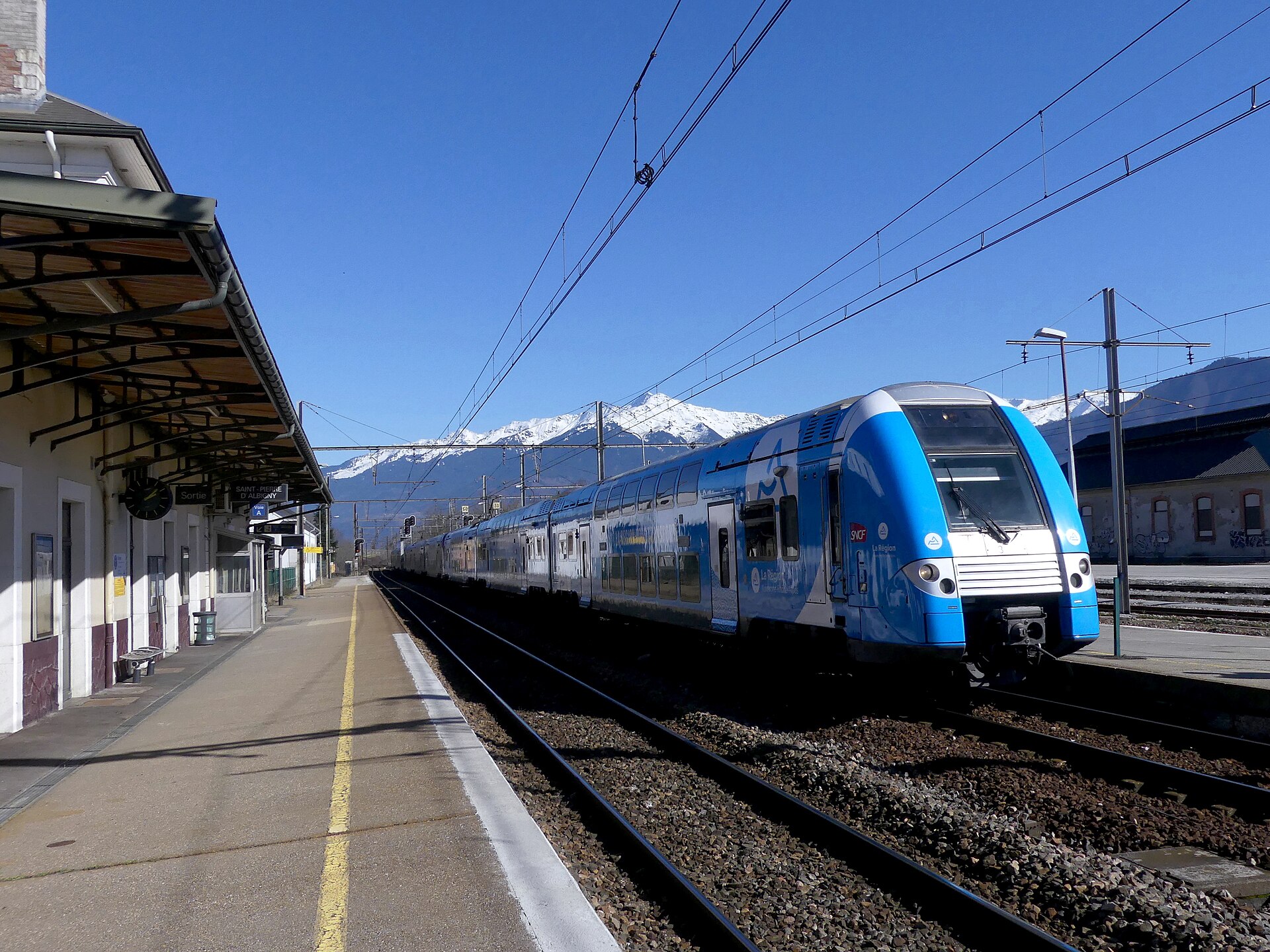 A blue TER train for Bourg-Saint-Maurice at a Savoie station with snow-covered peaks behind
