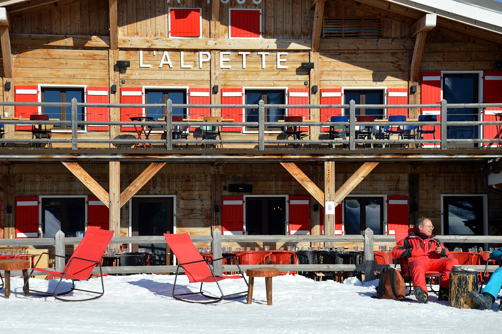 The timber facade and snowy sun terrace of the L'Alpette mountain restaurant above Megève, with red deckchairs on the snow