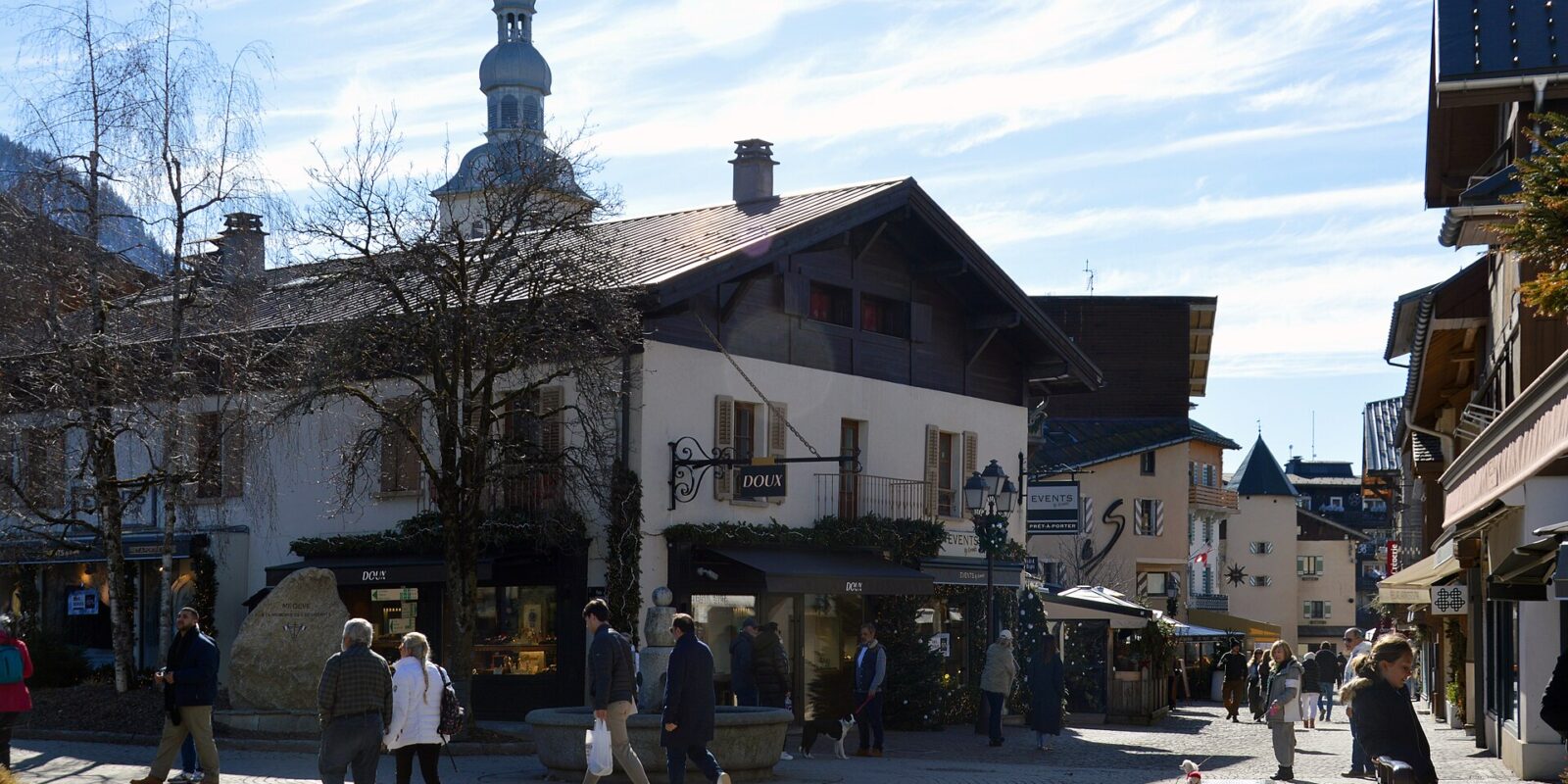The cobbled centre of Megève on a sunny winter day, with boutiques, a stone fountain, the onion-domed church tower and people walking