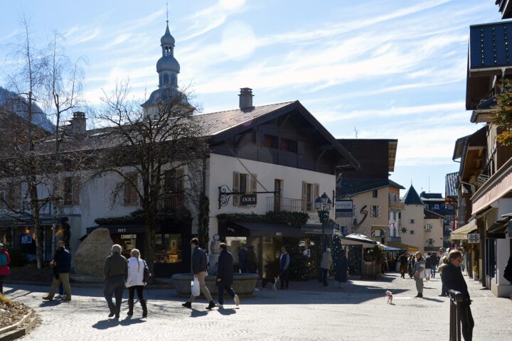 The cobbled centre of Megève on a sunny winter day, with boutiques, a stone fountain, the onion-domed church tower and people walking