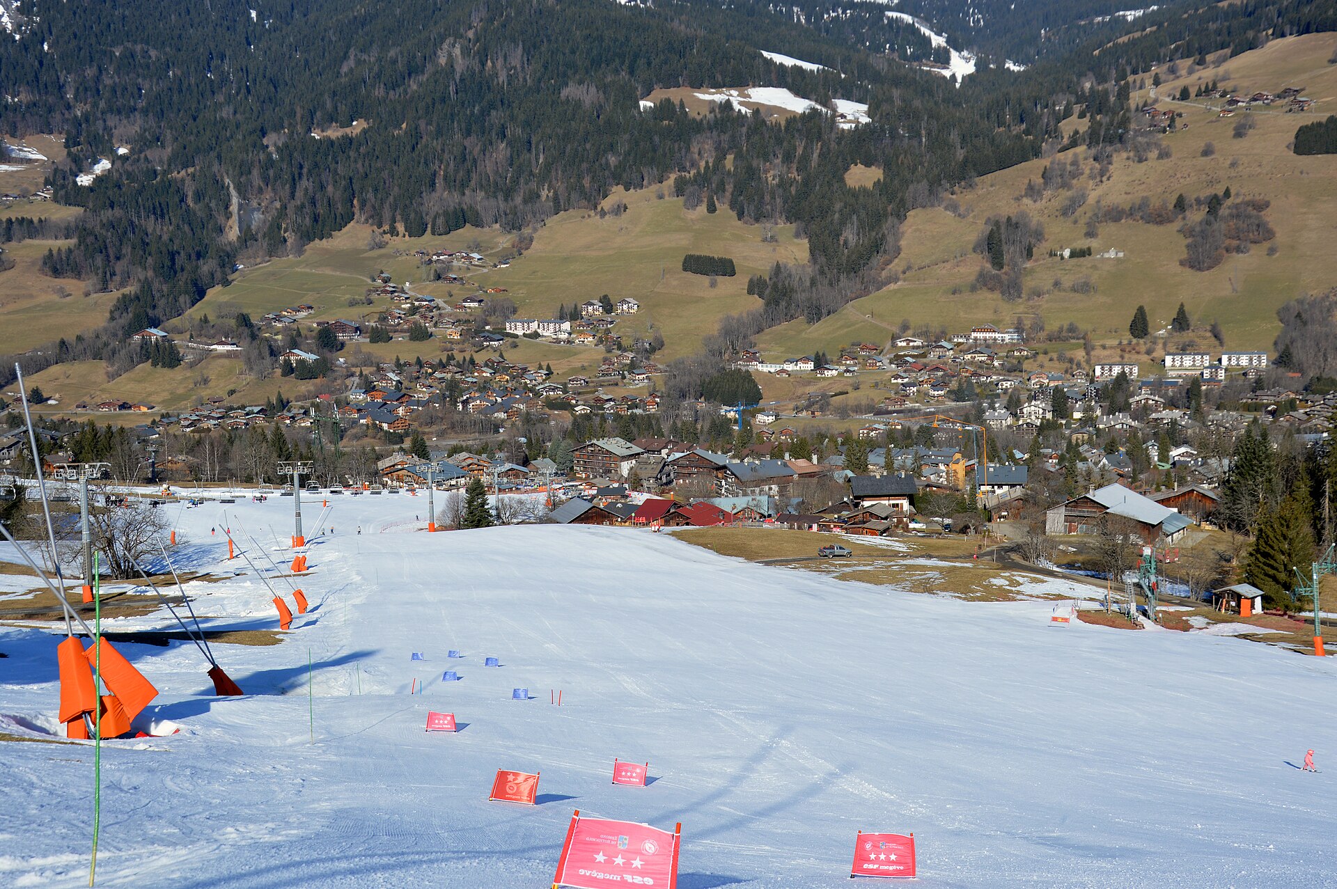 Looking down a thinly covered piste to the Rochebrune front de neige at Megève, with green fields on the hillside opposite