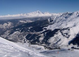 The Méribel valley under snow seen from the pistes above, with the resort's neighbourhoods on the hillside and Mont Blanc on the horizon