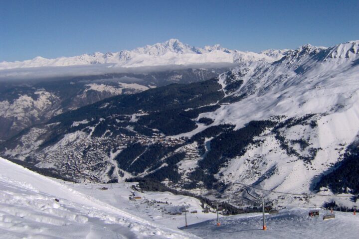 The Méribel valley under snow seen from the pistes above, with the resort's neighbourhoods on the hillside and Mont Blanc on the horizon