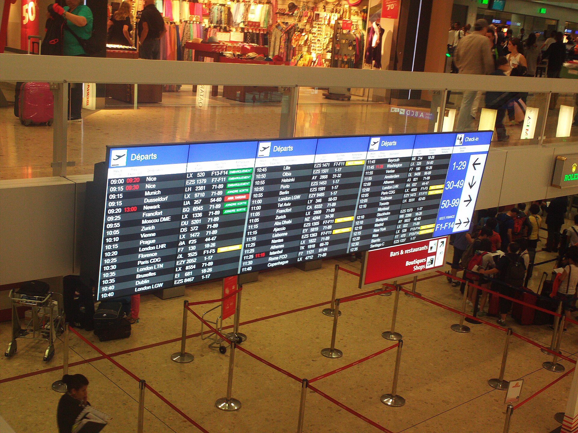 The check-in hall at Geneva Airport with a departure board and desk numbering above the queues