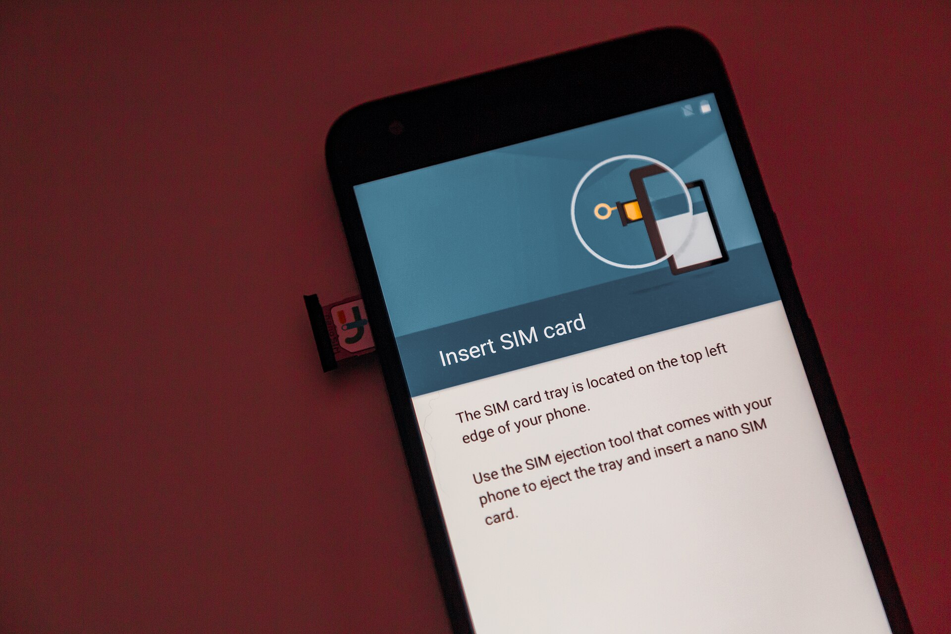 An Android phone displays SIM insertion instructions while a physical SIM card sits in its partly extended side tray.