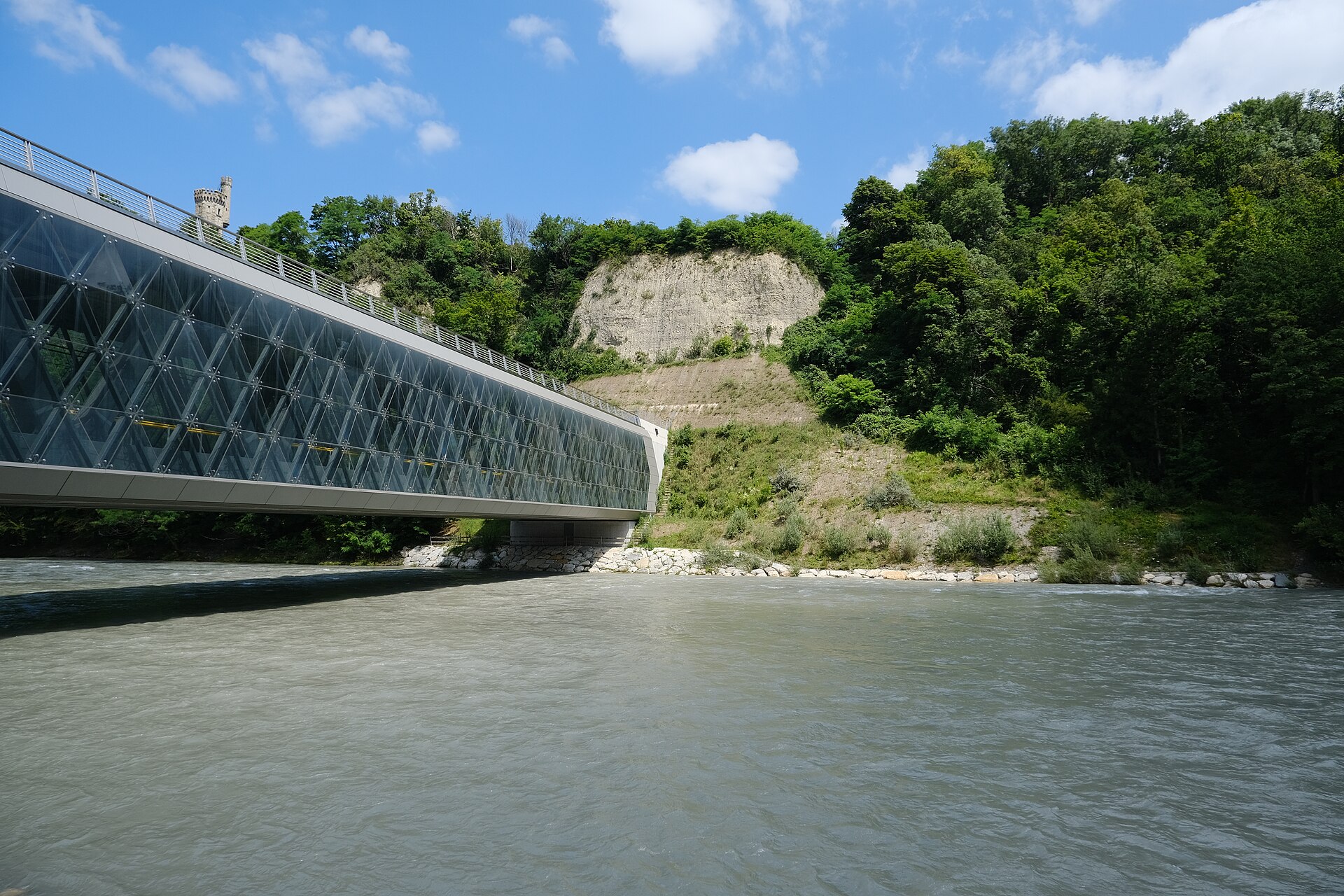 The Arve flows below the wooded Champel cliff in Geneva, beside the glazed Pont des Artisanes and the tower above.
