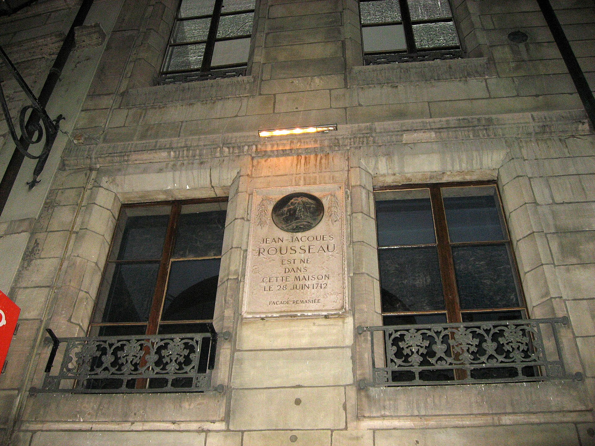 The birthplace plaque for Jean-Jacques Rousseau between iron balconies on the stone facade of Maison Rousseau in Geneva.