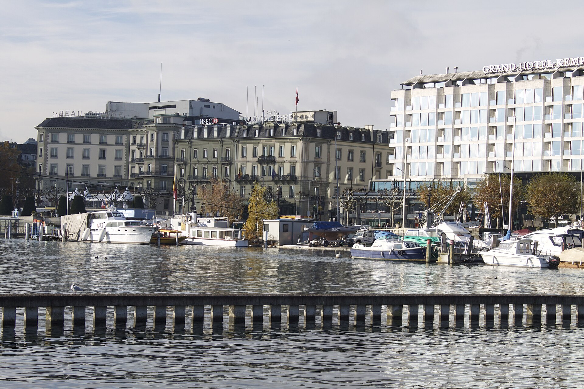 Boats line Geneva's waterfront below Beau-Rivage, Hôtel d'Angleterre and the Grand Hotel Kempinski in autumn sunshine.