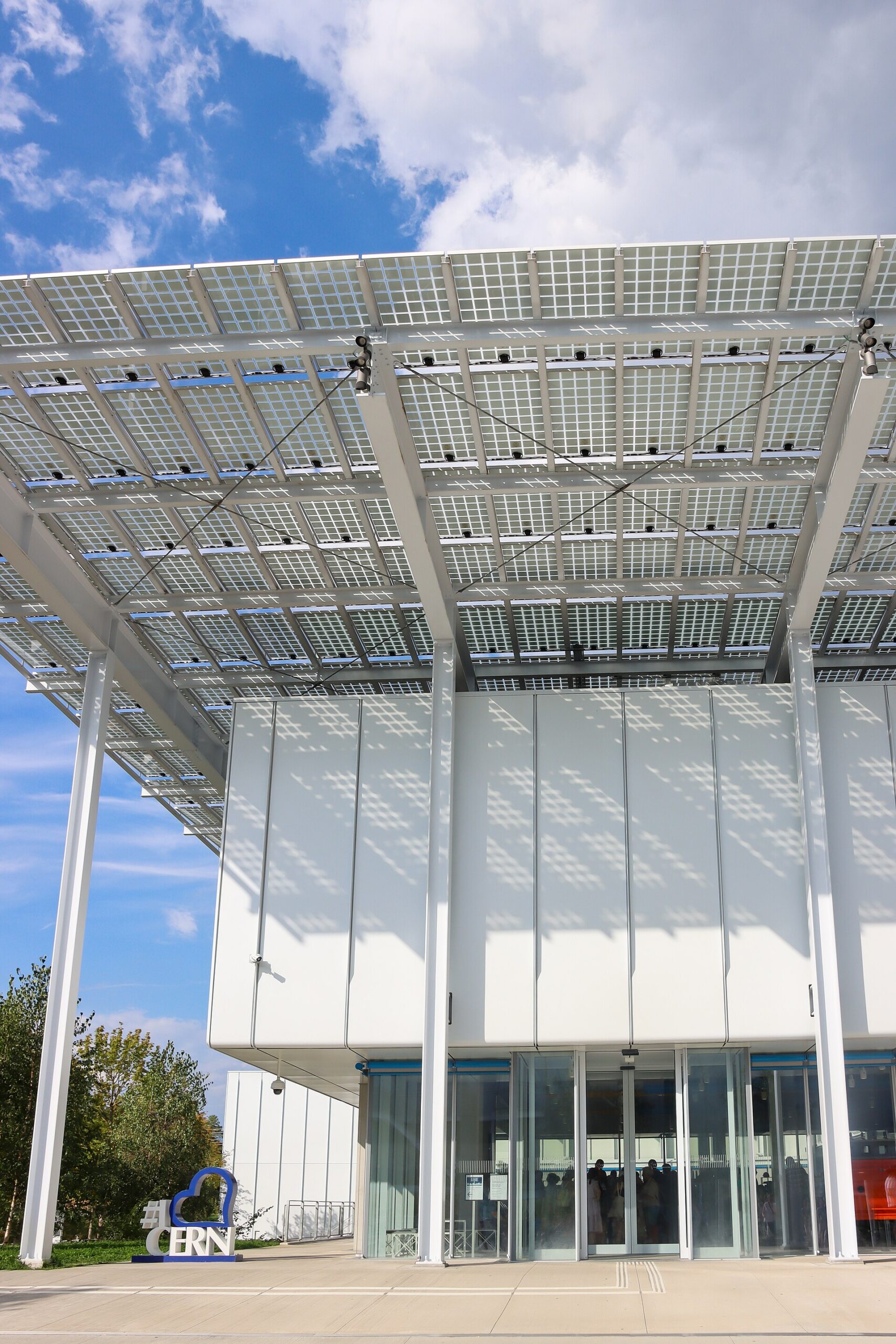 A broad gridded canopy shades the white facade and glass entrance doors at CERN Science Gateway in Meyrin.