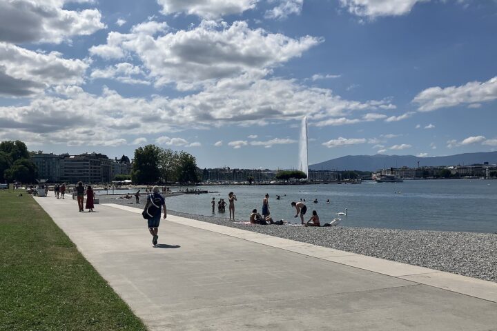 A broad promenade follows Plage des Eaux-Vives beside bathers in Lake Geneva, with the Jet d'Eau beyond.