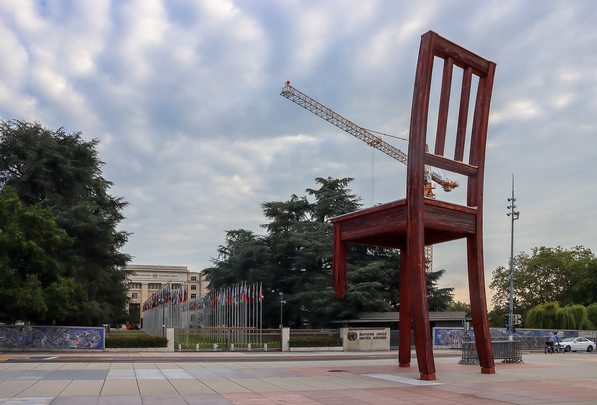 Broken Chair stands on Geneva's Place des Nations, with United Nations flags and the Palais des Nations behind it.