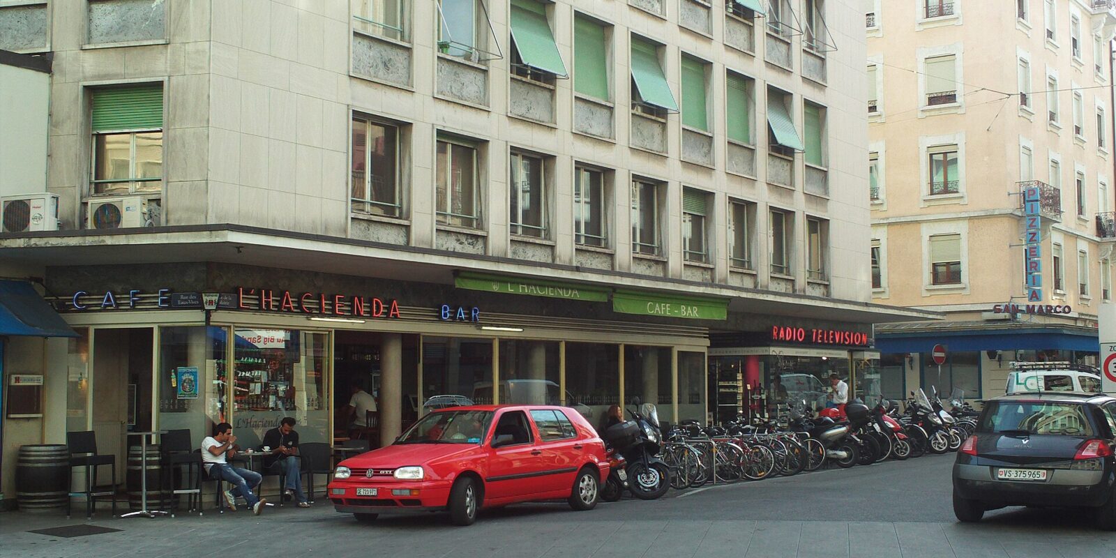 Cafe L'Hacienda has outdoor tables beneath its signs at a street corner in Geneva's Eaux-Vives district.