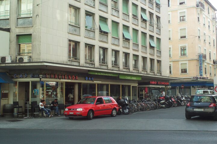 Cafe L'Hacienda has outdoor tables beneath its signs at a street corner in Geneva's Eaux-Vives district.