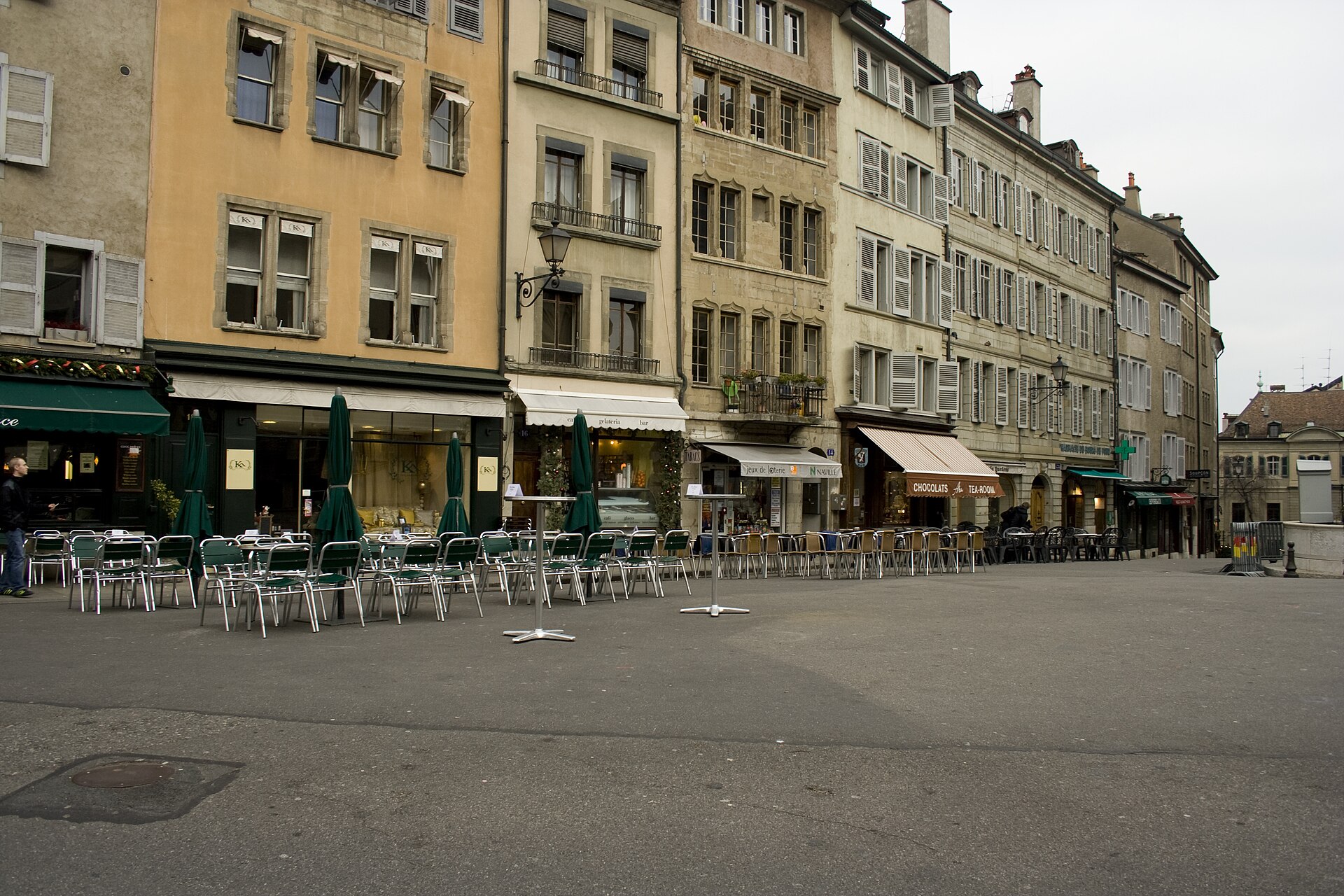Cafe tables and chairs line Place du Bourg-de-Four beneath the shuttered facades of Geneva Old Town.