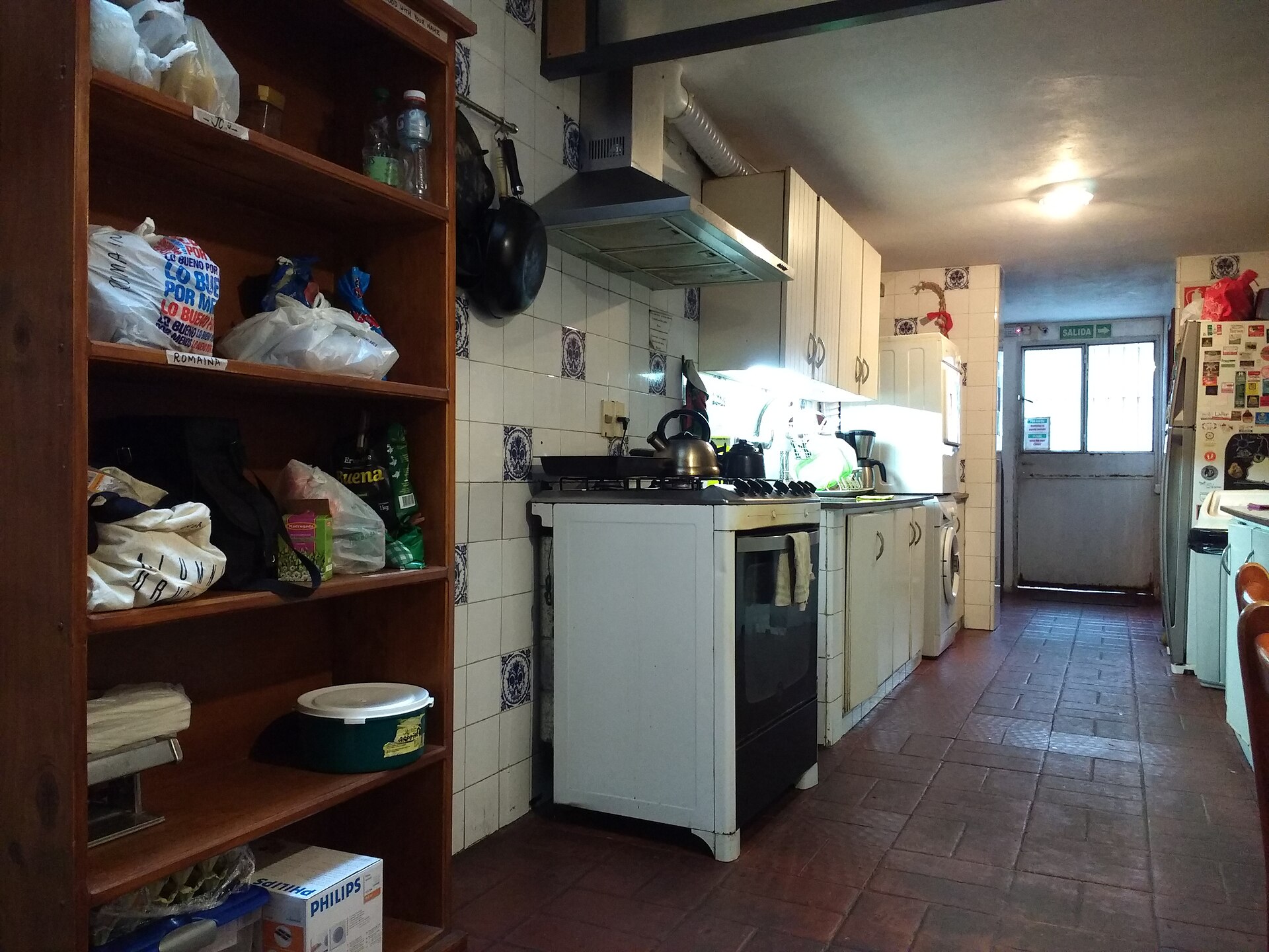 A cooker, sink, refrigerator and shelves of food bags fill the shared kitchen at Destino26 hostel in Montevideo.