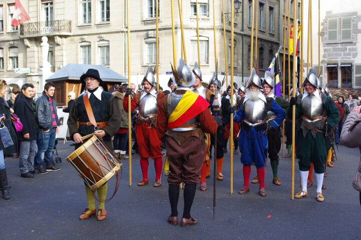 Costumed pikemen in steel helmets and breastplates stand with long pikes and a drummer on a Geneva street during the Escalade celebrations.