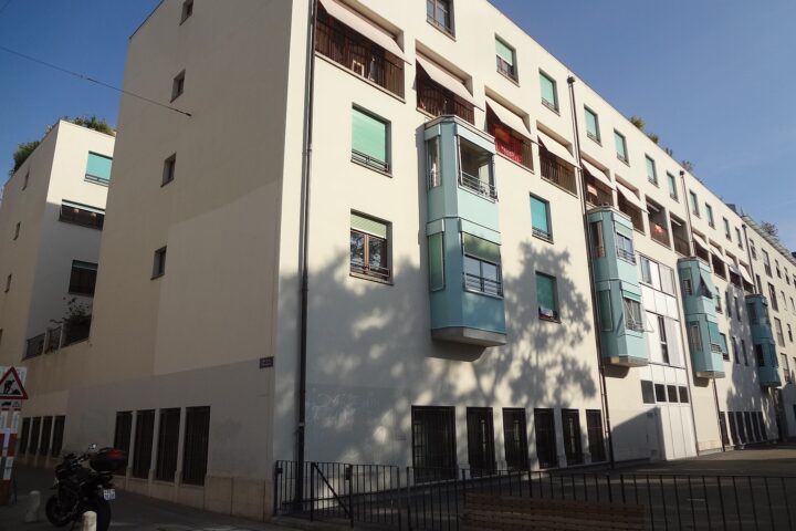 A cream apartment block in Geneva's Pâquis district has pale green projecting window bays, recessed balconies and green blinds.