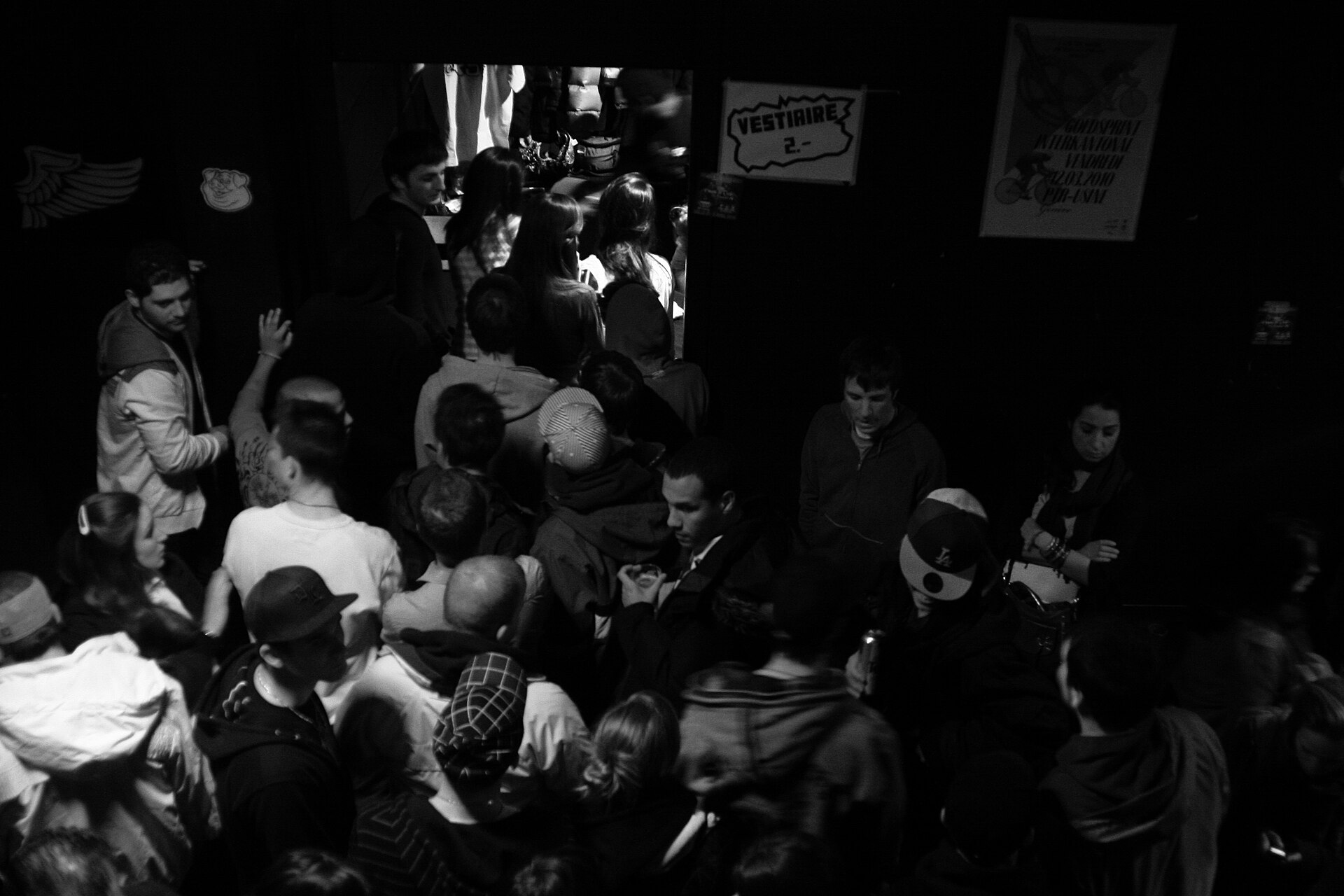 A crowd gathers beneath a cloakroom sign inside Le Rez at L'Usine in Geneva, in a monochrome club scene.