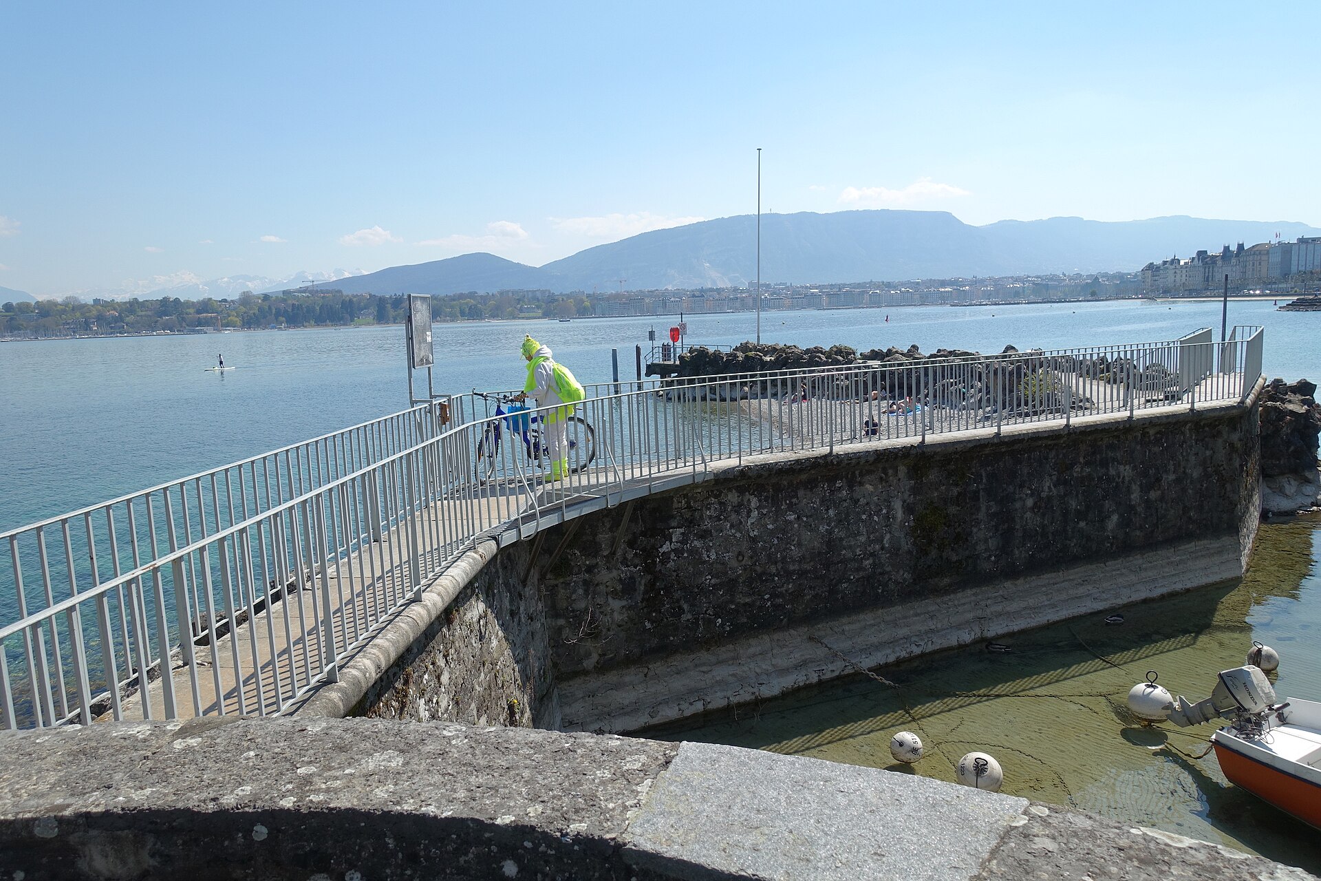 A cyclist passes the stone landing at Perle du Lac in Geneva, with metal railings and the lake beyond.