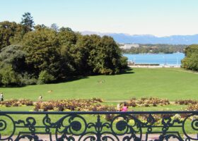 A decorative terrace railing frames flower beds and sunny lawns descending toward Lake Geneva from Parc La Grange in September.