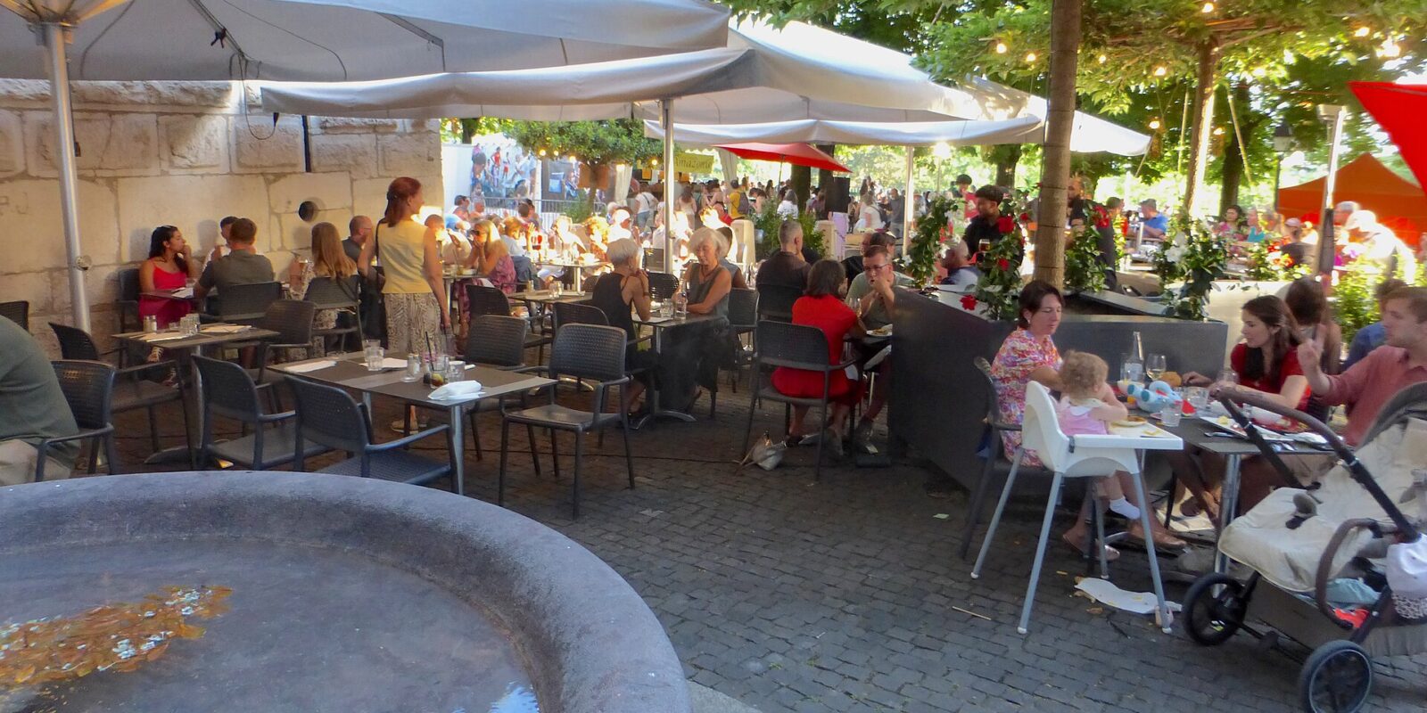 Diners fill Café Papon's shaded Geneva terrace beside a stone fountain during the Fete de la musique.
