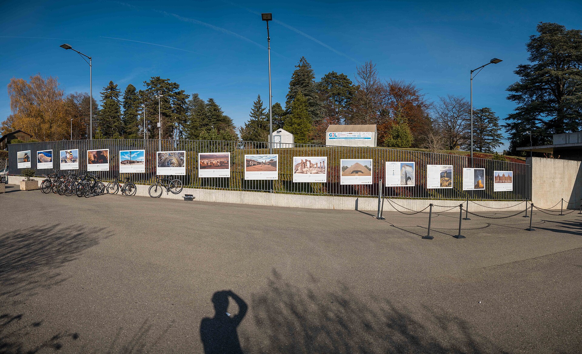 Exhibition panels line the fence beside bicycles and queue barriers at the United Nations Pregny gate in Geneva.
