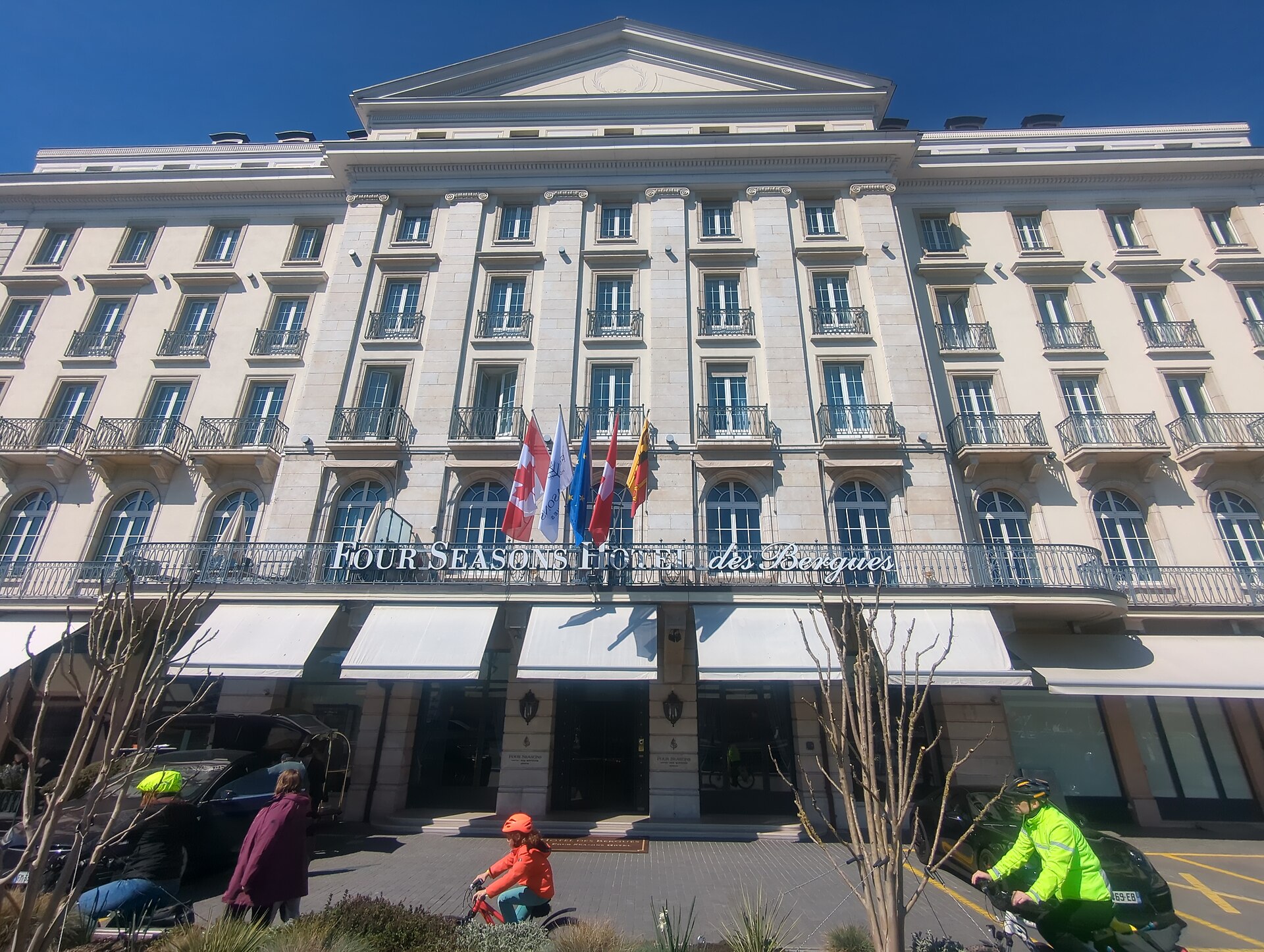 Flags and the Four Seasons Hôtel des Bergues name mark the entrance beneath a pale stone facade in Geneva.